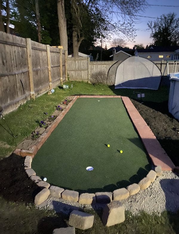Custom backyard golf putting green at dusk with brick border and golf balls - Big Moss Commander Bulk Turf  - ALLBGT