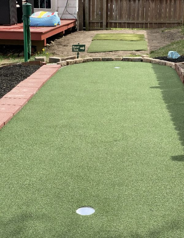 Outdoor putting green with red brick edging and “Next tee” sign - Big Moss Commander Bulk Turf custom install  - ALLBGT