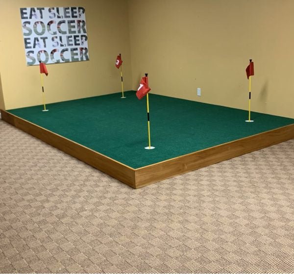 Elevated Big Moss V2 Bulk Turf putting green with four red flags in indoor sports room - ALLBGT