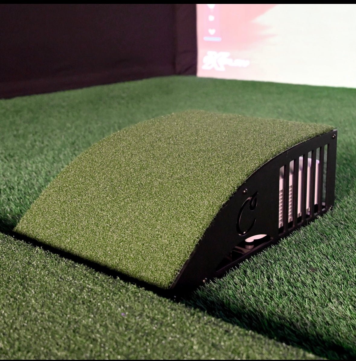 “Carl’s Place Floor-Mounted Projector Enclosure Kit positioned on simulator turf with curved protective cover - ALLBGT.”
