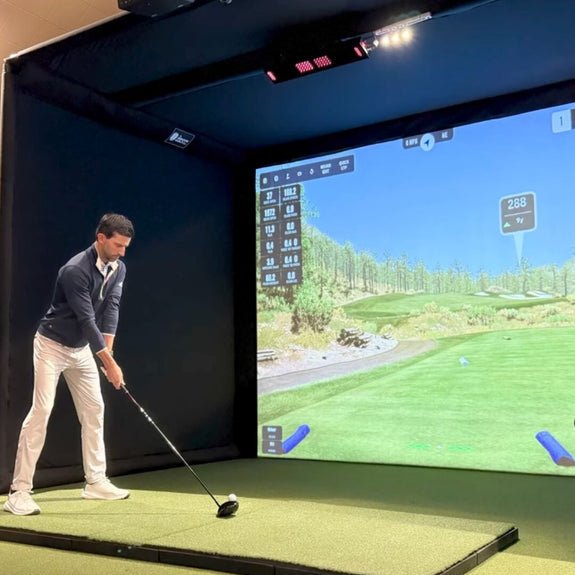 Man playing golf in a simulator with a large screen displaying a virtual golf course.